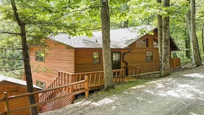 A cabin with a wooden exterior, a porch, and a gravel driveway.