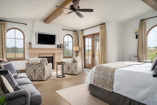 A spacious bedroom with a large bed, two armchairs, a fireplace, and a TV mounted on the wall. - Grand Reserve Inn (Plymouth)