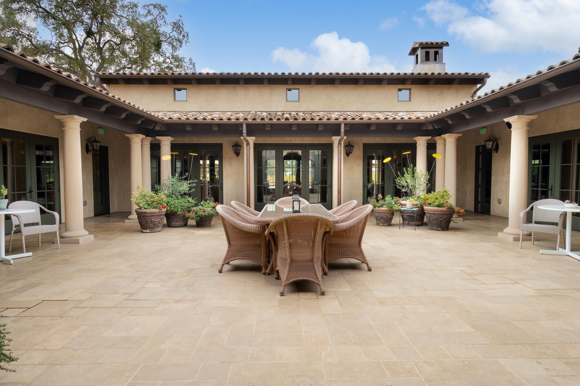 A courtyard with a central dining area featuring wicker furniture and potted plants.
