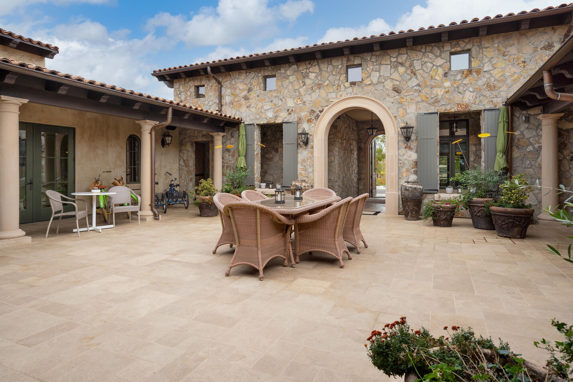 A courtyard with a stone building, wicker furniture, and potted plants.