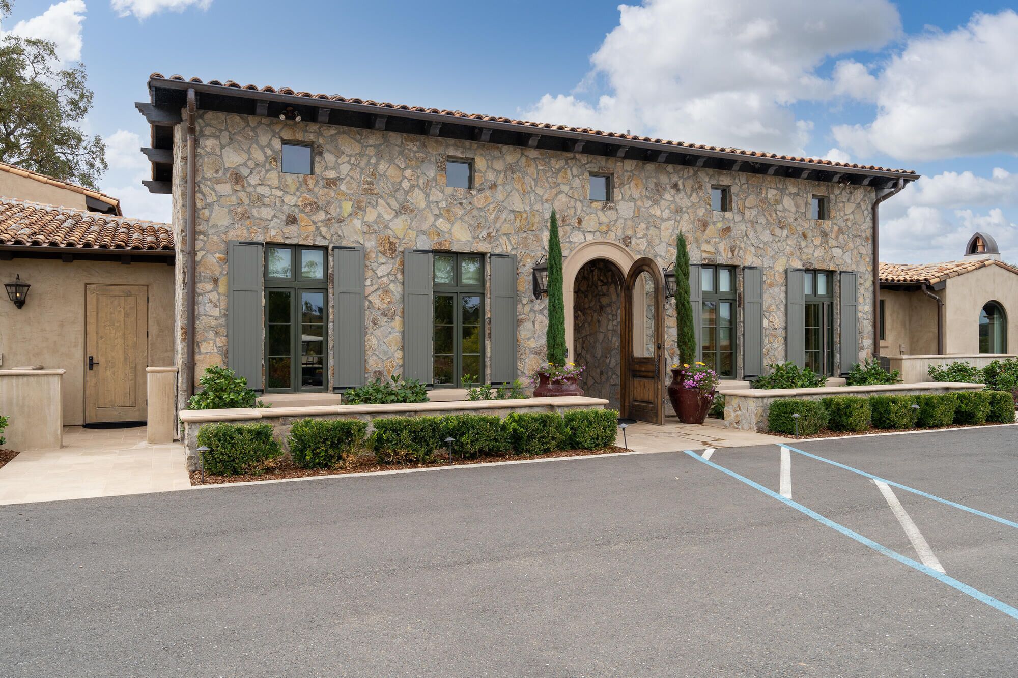 A stone building with a tiled roof, a central entrance with a door, and windows with shutters.