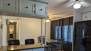 A compact kitchen with white cabinets, a wooden countertop, a dining table with chairs, a ceiling fan, and a refrigerator. - Riverfront Home (Tidioute)