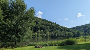 A grassy area with a small building near a lake, surrounded by dense forest and hills. - Riverfront Home (Tidioute)