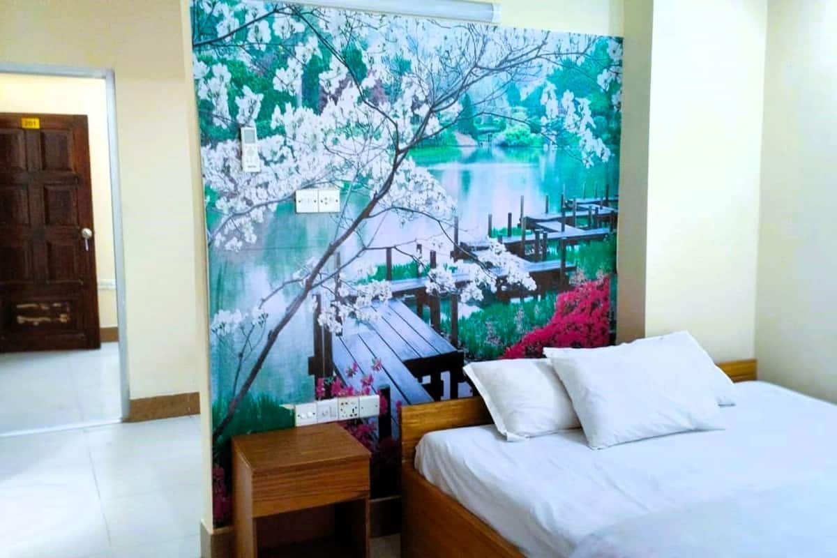 Ein Schlafzimmer mit einem Bett, einem Nachttisch aus Holz, einem an der Wand befestigten Fernseher und einer Tür mit einer Nummer.