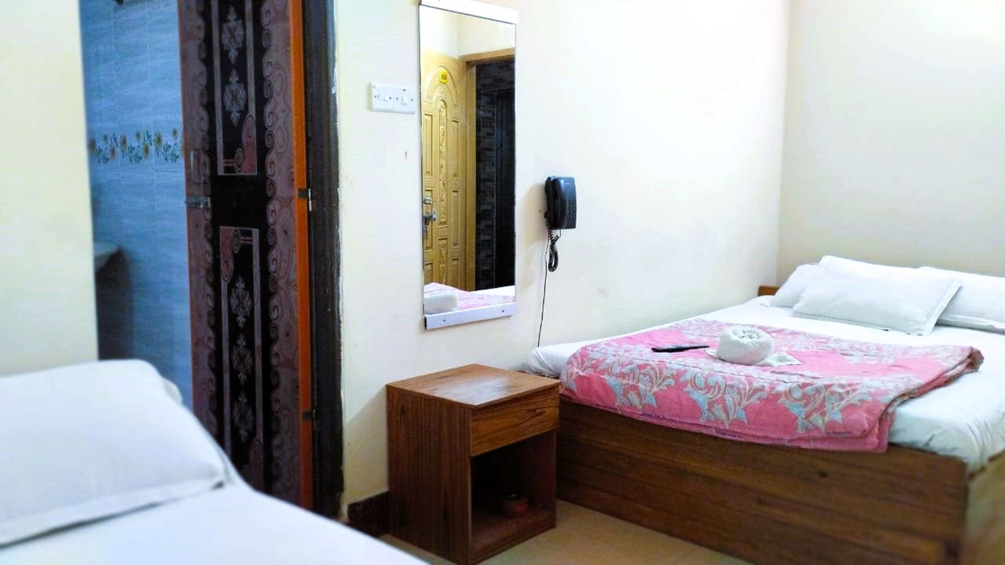 Un dormitorio con cama, mesita de noche, espejo y teléfono.