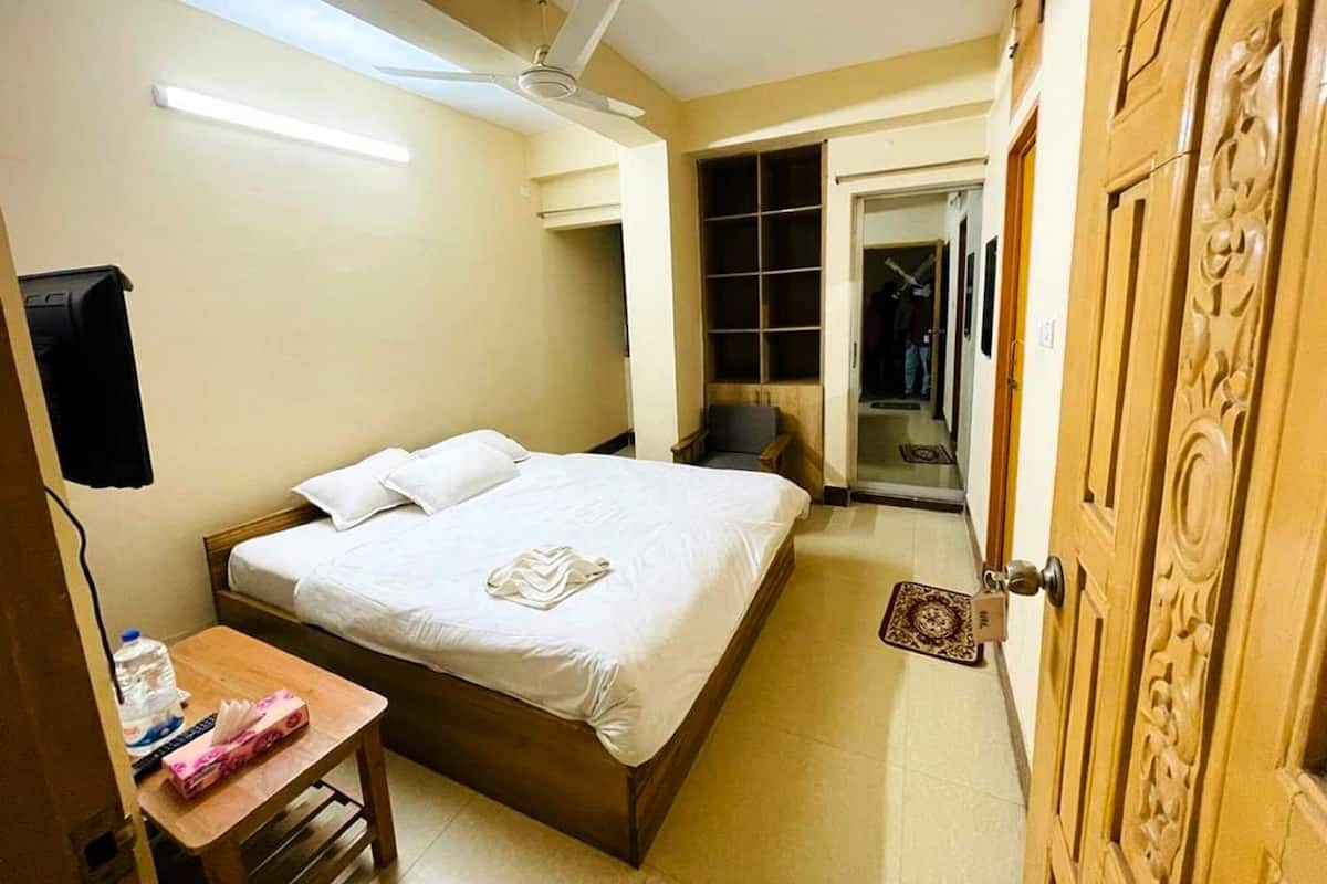 Ein Hotelzimmer mit einem Bett, einem Schreibtisch, einem Deckenventilator, einem Kleiderschrank und einer Tür mit aufwendigen Schnitzereien.