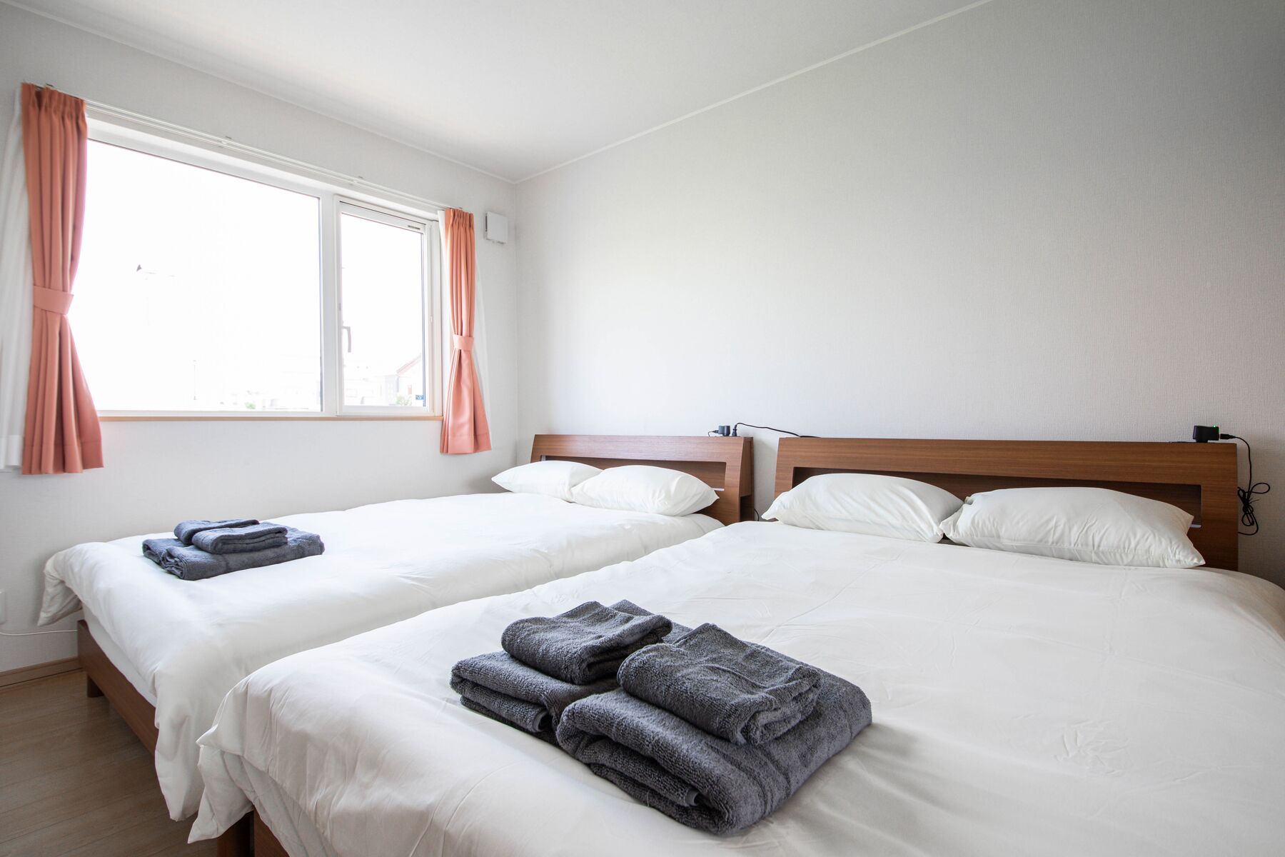 A hotel room with two beds, each with white bedding and pillows. There are folded towels on the beds, and a window with curtains.