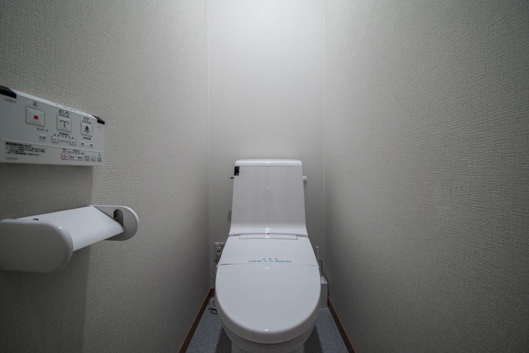 Et lille, enkelt badeværelse med toilet, håndtørrer og et panel på væggen.