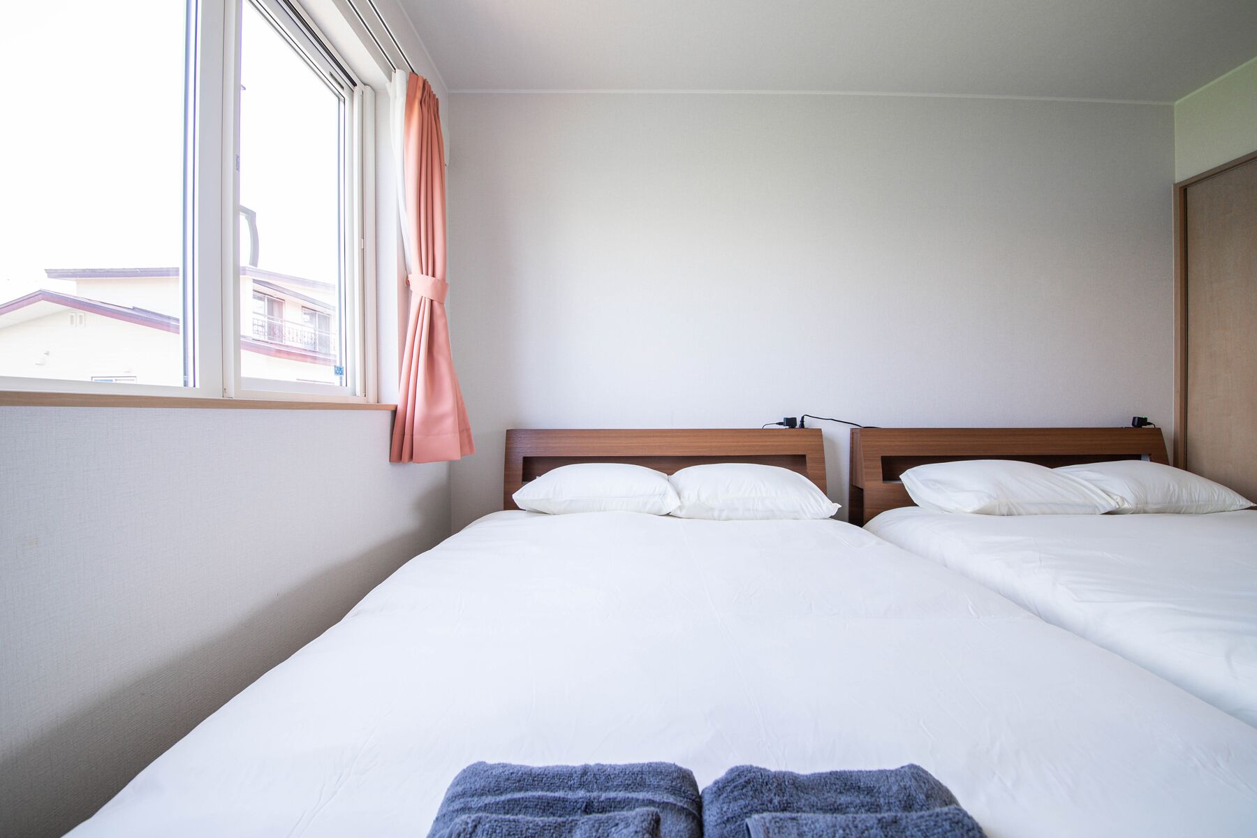 A hotel room with two beds, a window with curtains, and a view of buildings outside.
