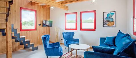 A modern living room with a wooden staircase, blue furniture, and large windows.