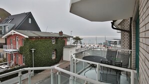 Ein Balkon mit Glastisch und Stühlen, mit Blick auf eine Wohngegend mit einem Backsteinhaus und einem roten Gebäude.