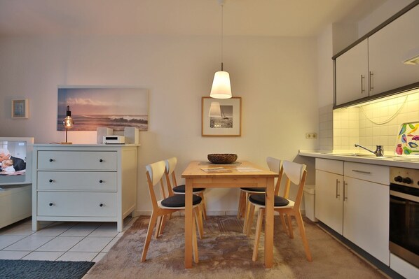 Una cocina compacta con zona de comedor, que incluye una mesa de madera, sillas, una lámpara colgante y un salpicadero de azulejos.