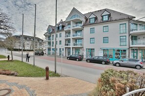 Un immeuble résidentiel à plusieurs étages, doté de balcons, d’un trottoir pavé et de voitures garées.