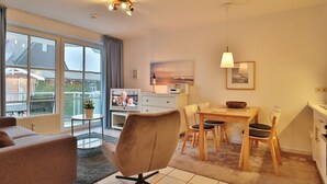 Ein modernes Wohnzimmer mit einer Couch, einem Esstisch mit Stühlen, einem Fernseher und einer Küchenzeile mit Spüle und Schränken.