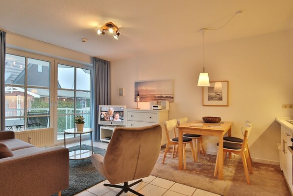 A modern living room with a sofa, a dining table with chairs, a TV, and a kitchen area with a sink and cabinets.