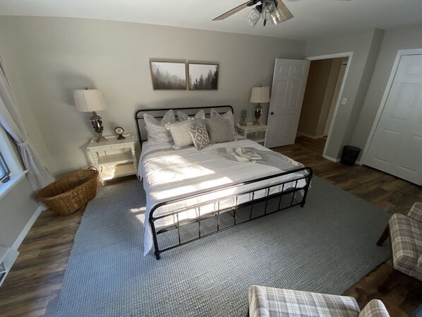 A bedroom with a bed, nightstands, a chair, a ceiling fan, and artwork on the wall. - Renovated House on Fence Lake for Families, Sunset View, Boat Dock, Snomo Access (Lac du Flambeau)