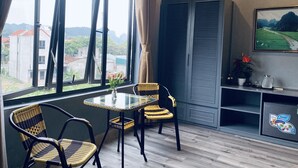 Una habitación con un ventanal grande, una mesa con sillas, un televisor en la pared y un mueble con una planta y una jarra.