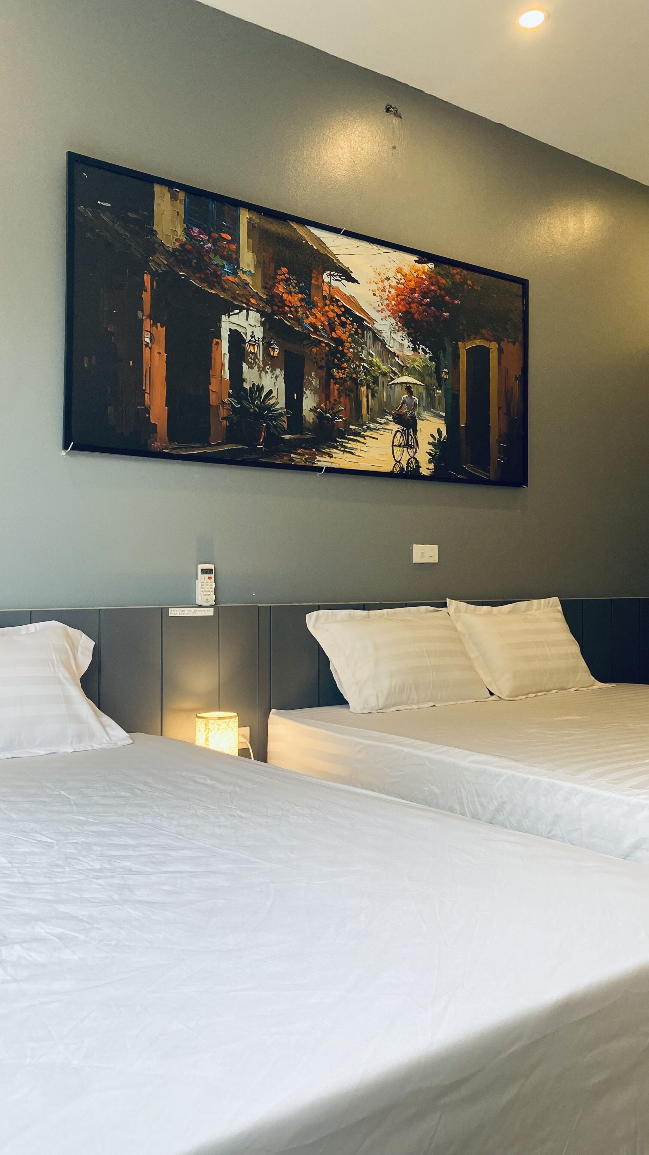 A hotel room with two beds, a large painting on the wall, and a bedside lamp.