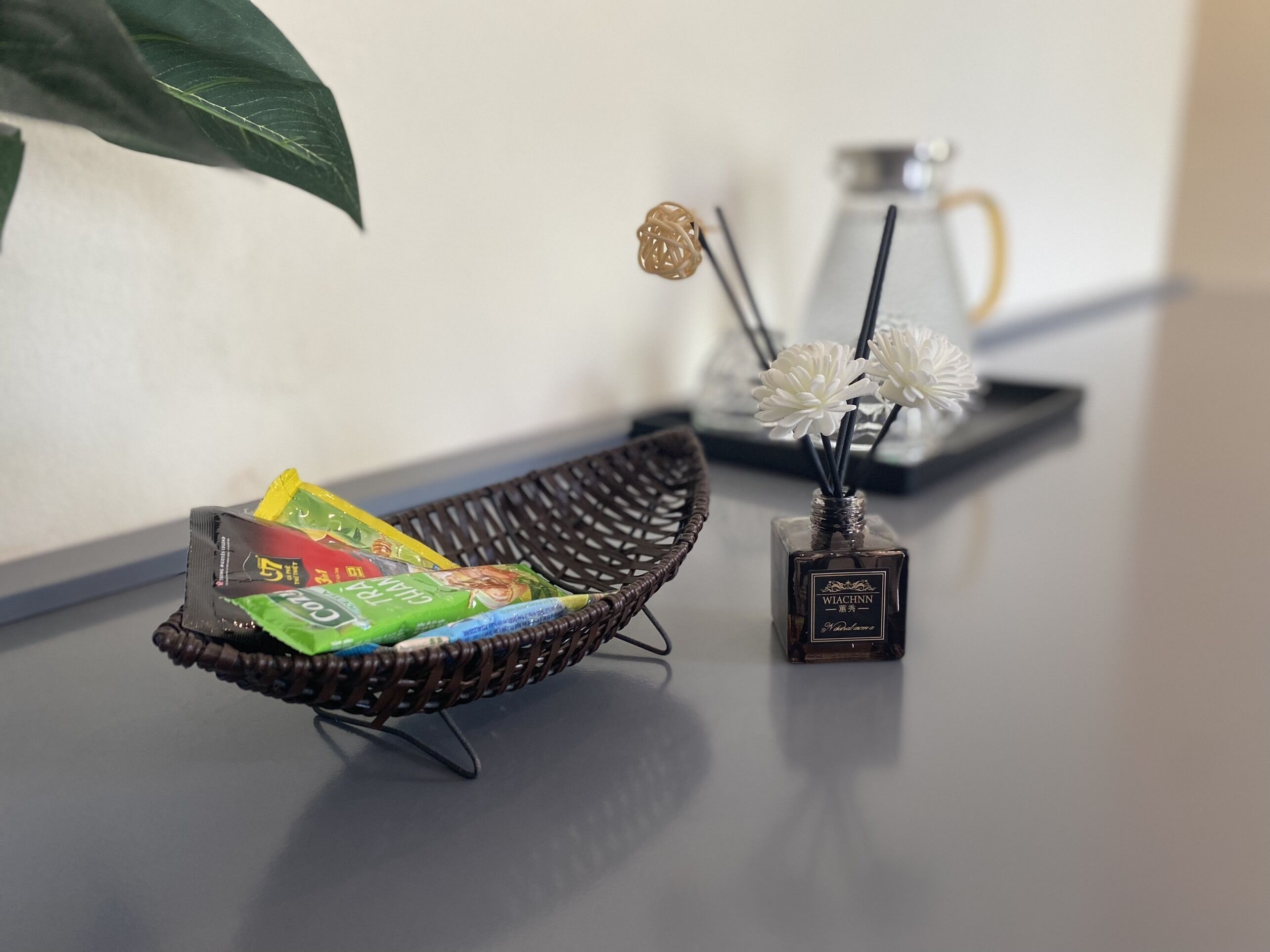 Un panier en osier contenant des emballages de collations, un petit vase avec des fleurs blanches et une machine à café sur une table.