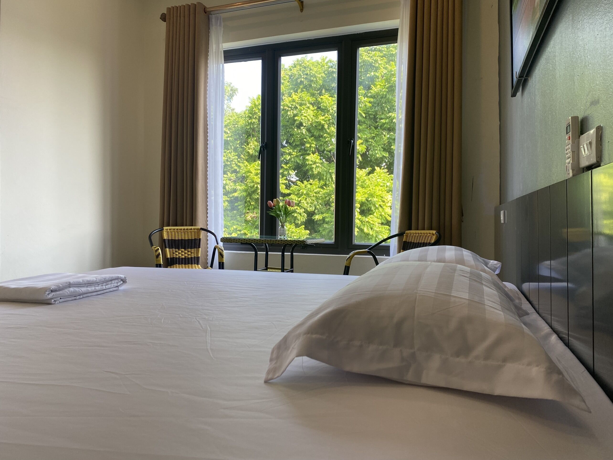 Ett hotellrum med en säng, två fåtöljer i rotting, ett litet bord och ett fönster med utsikt över träd.