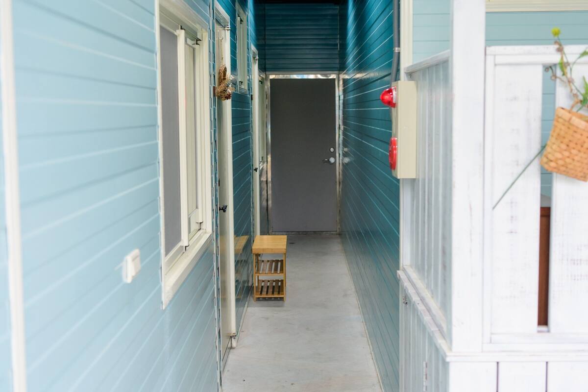 Un couloir étroit aux murs recouverts de lambris bleu clair, un banc en bois et une porte au fond.