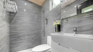 A modern bathroom with a white toilet, a shower area, and a sink with a mirror above it. - Little Lost B&B｜Family / Pet Friendly (Liuqiu)