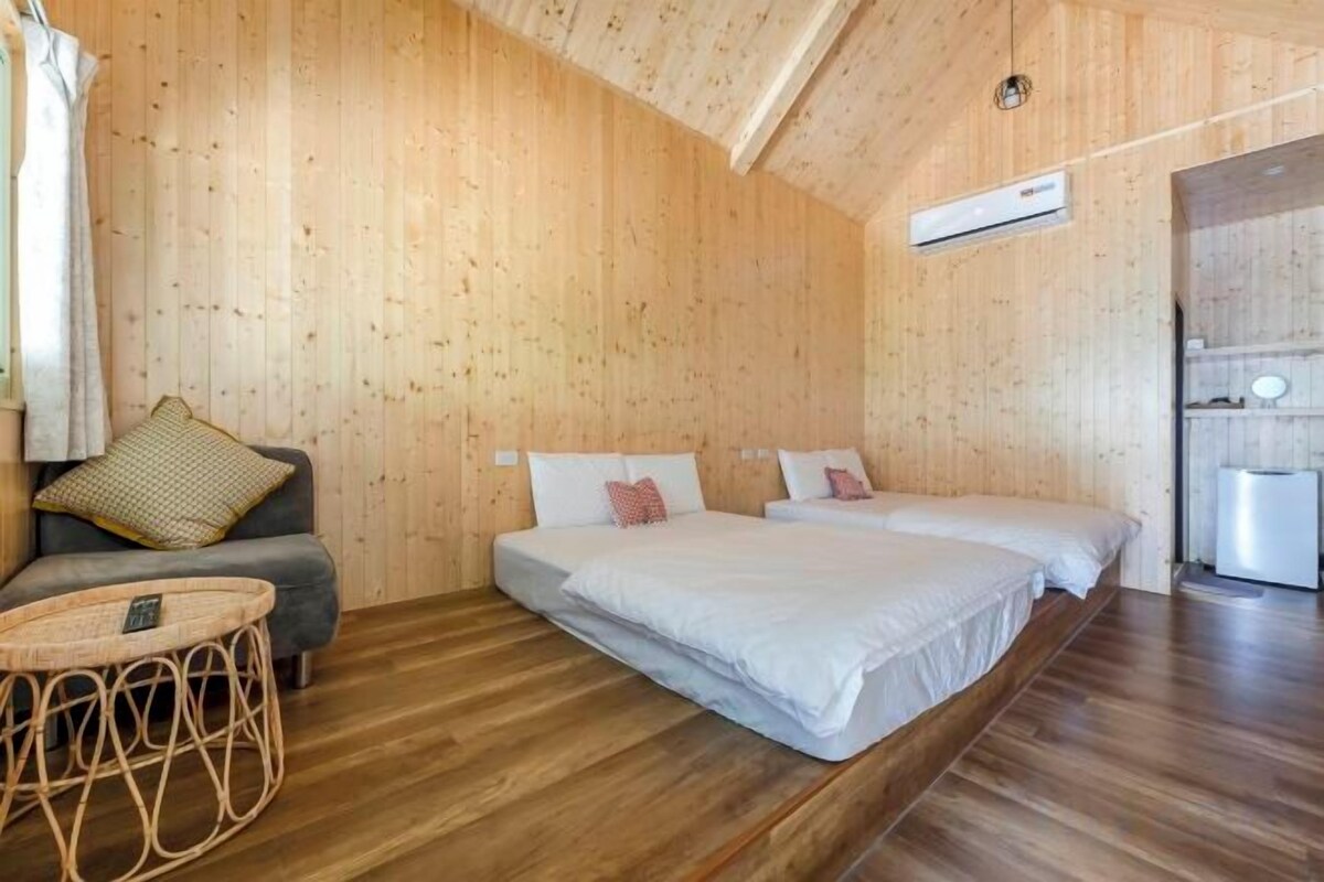 A wooden-paneled room with a bed, a sofa, a small round table, and a kitchenette area.