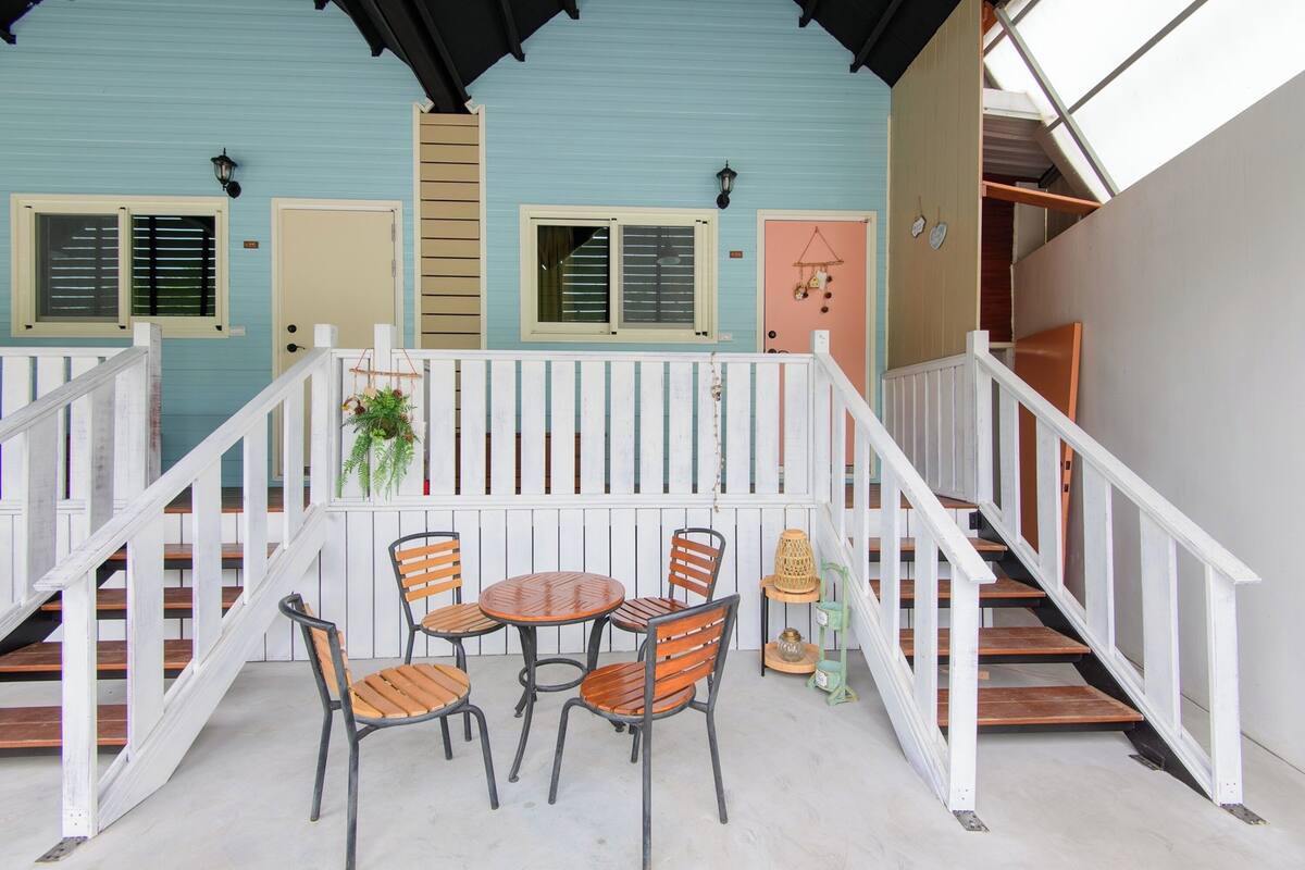 Un espace extérieur abrité, avec une rambarde blanche, une table en bois et des chaises.