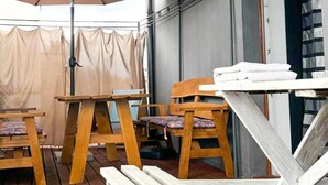 A wooden deck with tables and chairs, a covered area with a beige curtain, and a stack of white towels on a table. - Stunning home in Rybical with WiFi (Rybical)