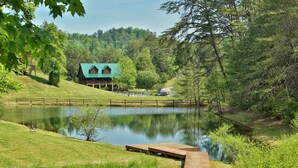 A cabin with a green roof, a wooden dock, and a pond in a wooded area. - Pool! View~Air Hockey~Fire Pit~Hot Tub~SemiSeclude (Sevierville)