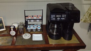 A coffee station with a coffee maker, jars of coffee, a sign that says "coffee helps," and a shelf with coffee cups and containers.