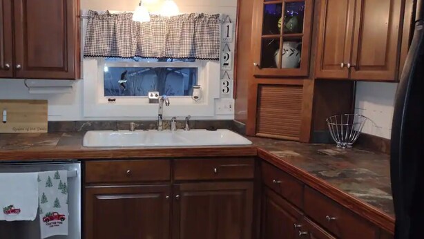 A kitchen with wooden cabinets, a white sink, and a window with a checkered valance.