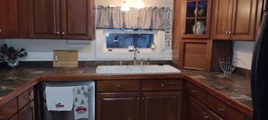 A kitchen with wooden cabinets, a white sink, and a window with a checkered valance. - Cozy, comfortable and close to Cleveland-Canton-Skiing & Cuyahoga Natl. Park (Akron)