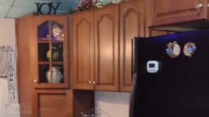 A kitchen with wooden cabinets, a black refrigerator, and a small island with a glass bowl.