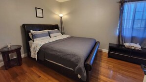 A bedroom with a bed, a bedside table, a floor lamp, a ceiling fan, and a window with curtains. - Family Fun Home (Beverly Hills)