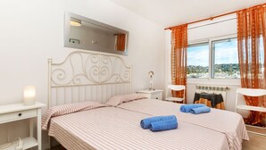 A hotel room with a bed, a nightstand, a desk, a chair, a window with curtains, and a view of the outside. - Cortijo Barques by Interhome (Sitges)