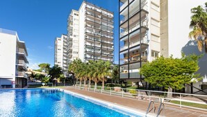 A swimming pool surrounded by modern apartment buildings with balconies, palm trees, and a clear blue sky. - Cortijo Barques by Interhome (Sitges)