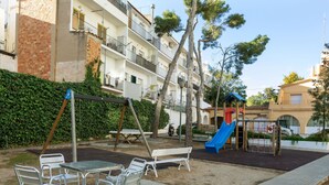 A courtyard with a playground, seating area, and a building with balconies. - Cortijo Barques by Interhome (Sitges)