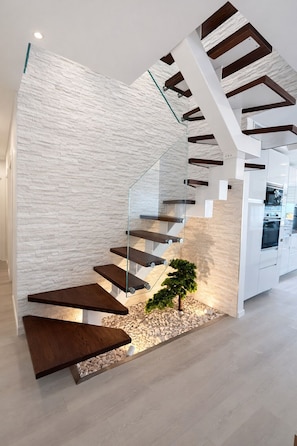 A modern staircase with glass railings and wooden steps, leading to a kitchen area.