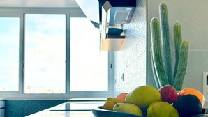 Una cocina moderna con un ventanal grande, un bol de fruta en la encimera y un cactus en la pared.
