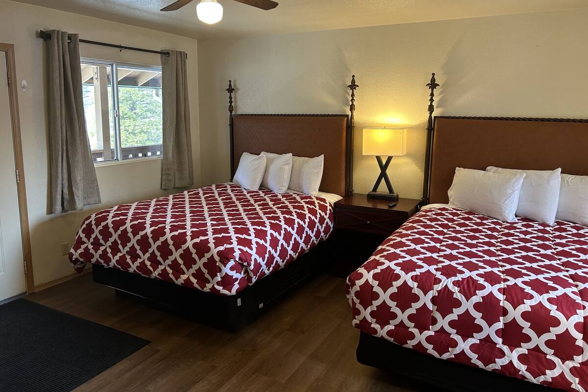 Une chambre d’hôtel avec deux lits, un ventilateur de plafond, une table de chevet avec une lampe et une fenêtre avec des rideaux.