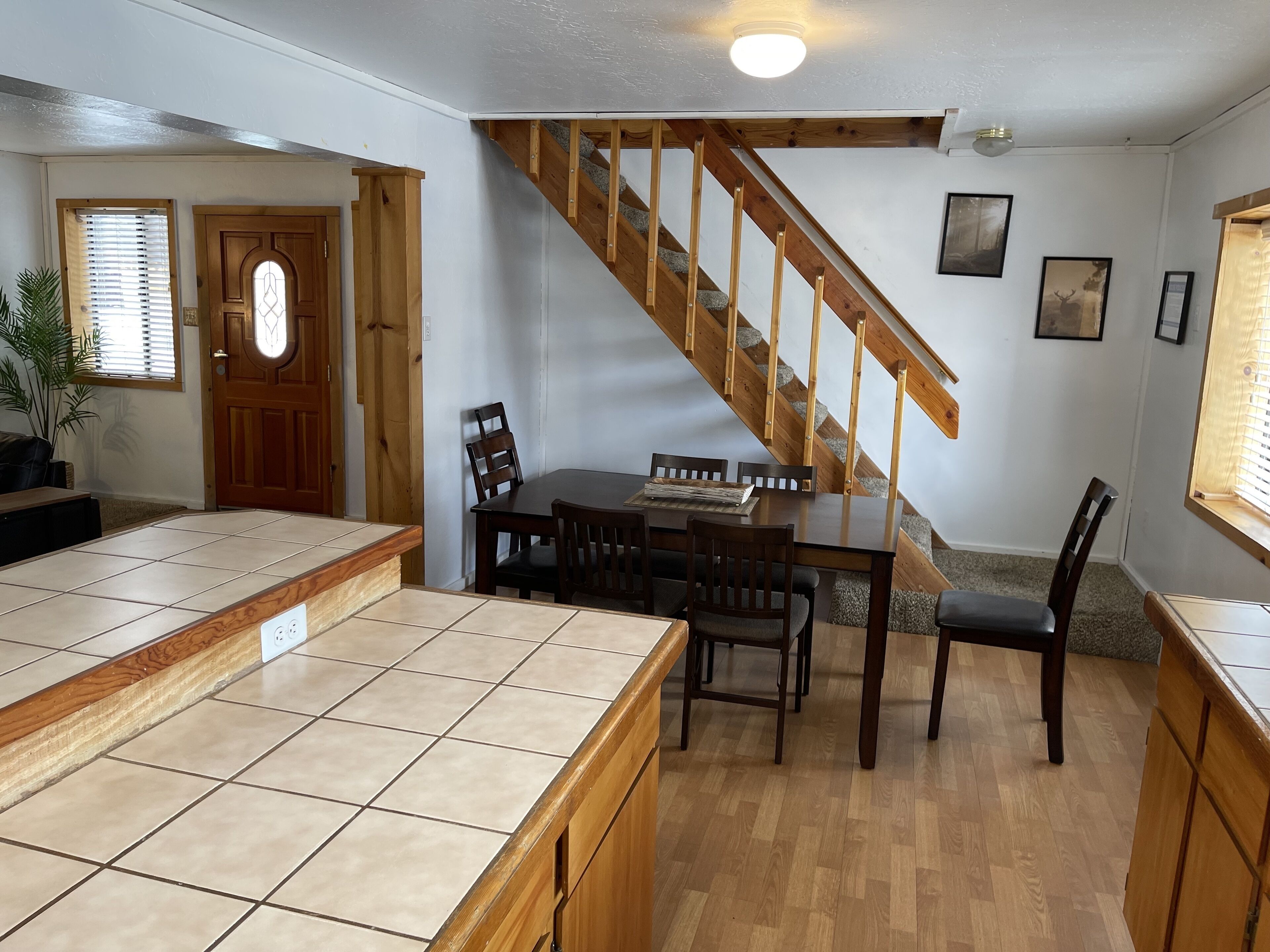 A kitchen with a wooden staircase, a dining table with chairs, and a tiled countertop.