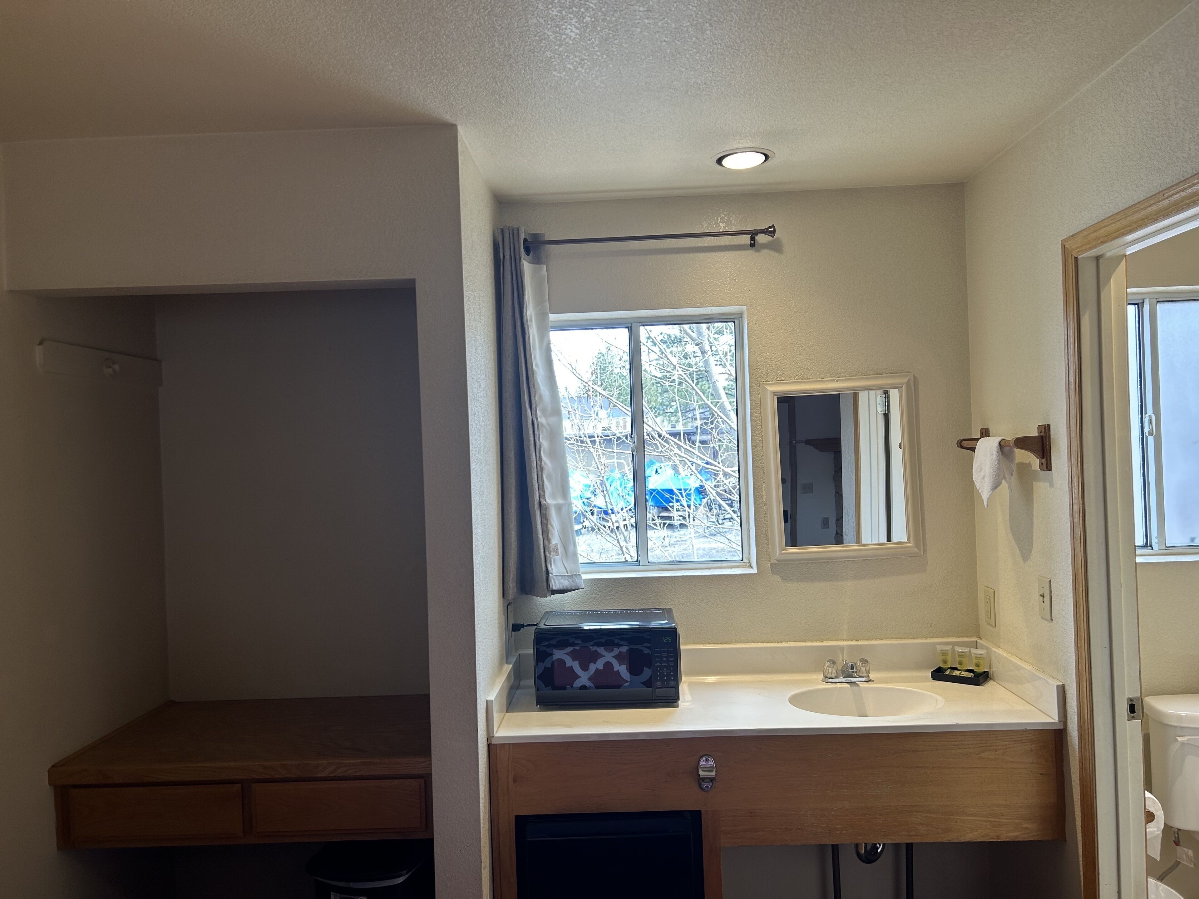 A compact bathroom with a wooden vanity, a window with a view of trees, a mirror, and a towel rack.