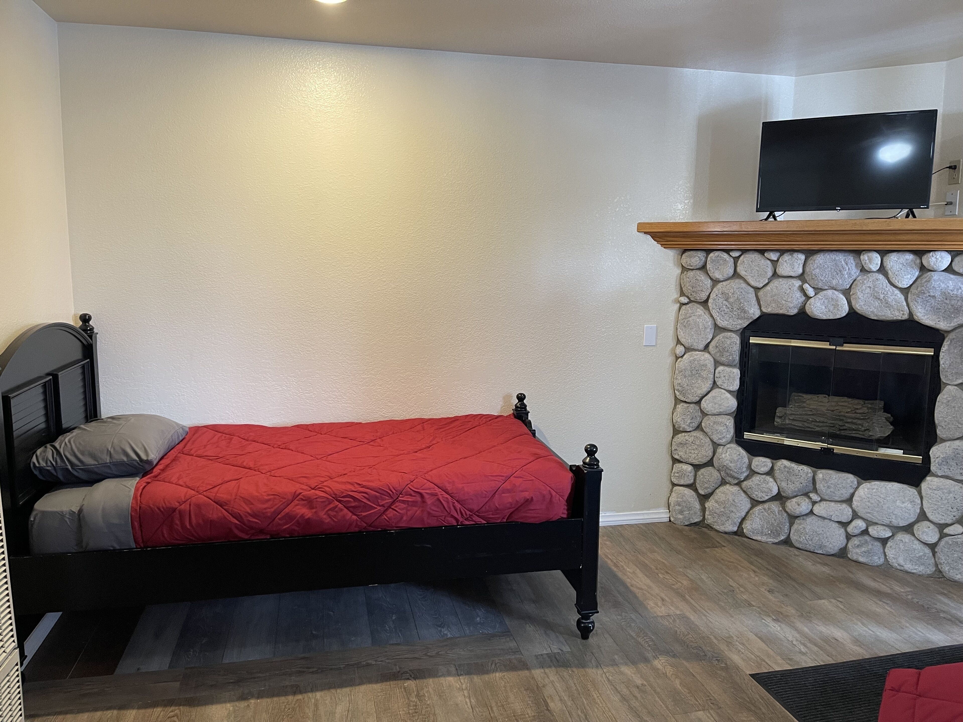 Ein Schlafzimmer mit einem Bett, einem Kamin aus Stein und einem Fernseher auf einem Schrank.