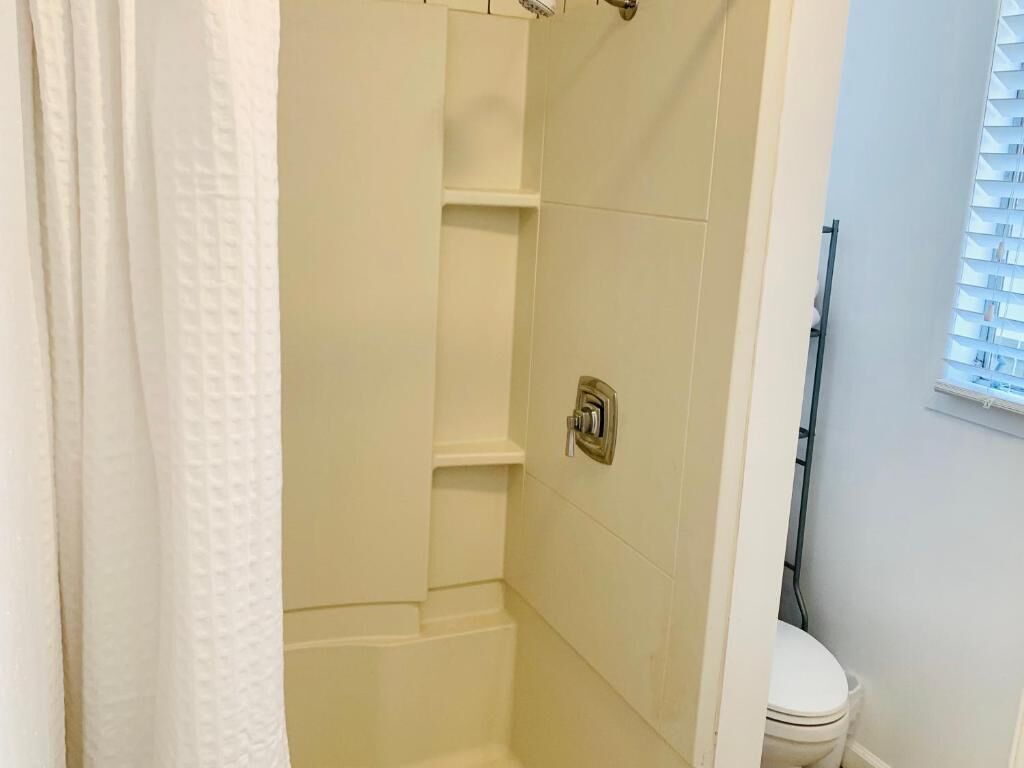 Une salle de bain avec douche, toilettes et une fenêtre équipée de stores.