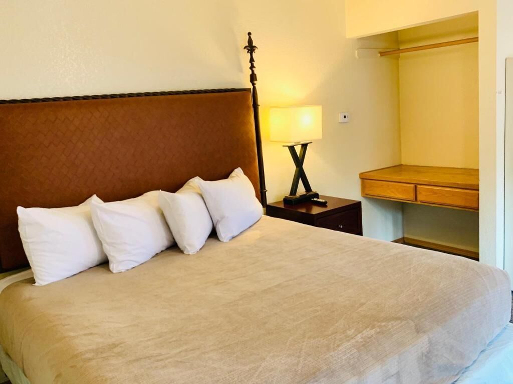 A neatly made bed with a brown headboard, a bedside lamp, and a wooden nightstand.