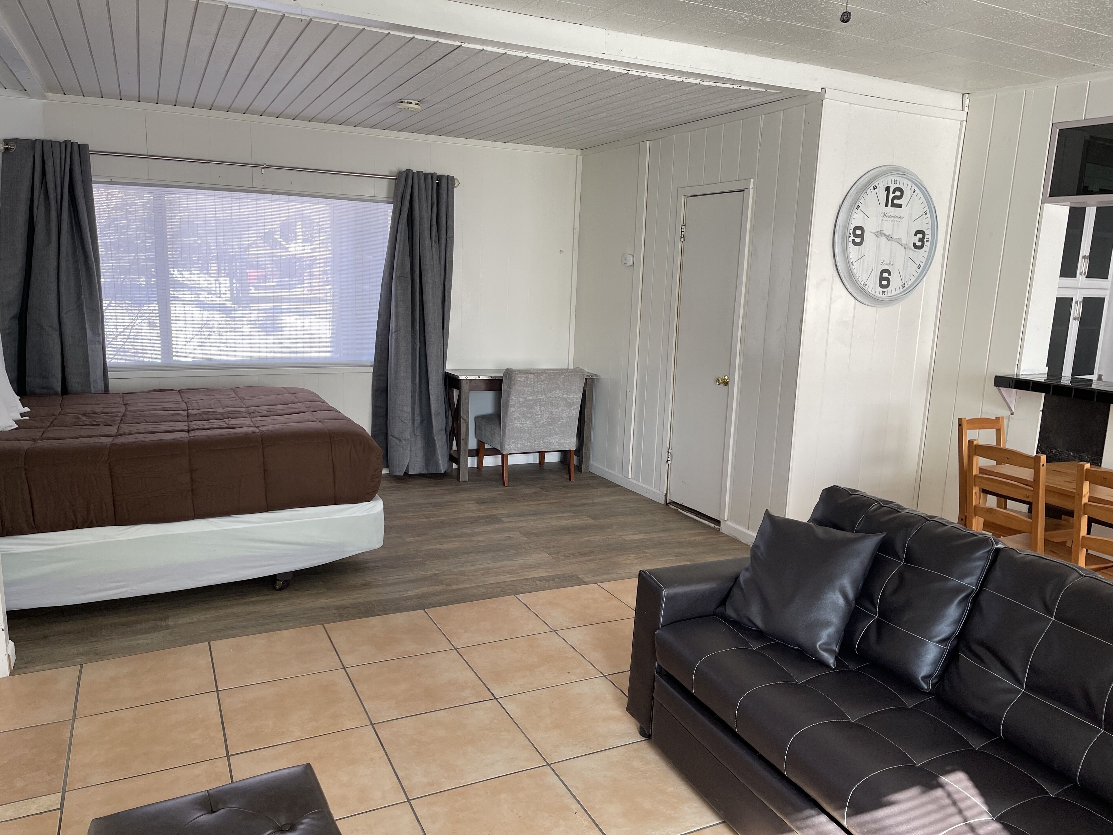 A bedroom with a bed, a sofa, a dining table, and a clock on the wall.