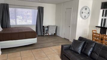 A bedroom with a bed, a sofa, a dining table, and a clock on the wall.