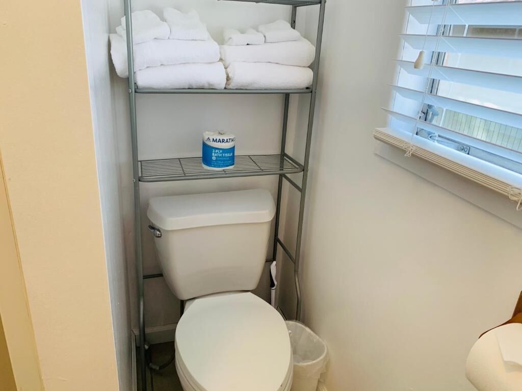 Un baño pequeño con un inodoro, un estante con toallas dobladas y un paquete de papel higiénico.