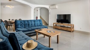 A modern living room with a blue sofa, a wooden coffee table, a TV on a wooden stand, and a staircase in the background.